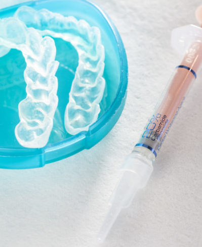 Two custom teeth whitening trays laying in a blue retainer case next to a container of bleaching gel
