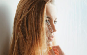 Side view of blonde woman looking anxiously away with half her face hidden by her hair because she is worried about acne