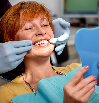 An older woman in a bright yellow shirt smiling during her teeth whitening consultation