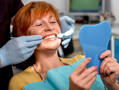 A woman with short red hair smiling as the dentist examines her teeth