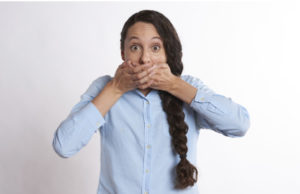 woman with a long, brown braid covering her mouth with both hands