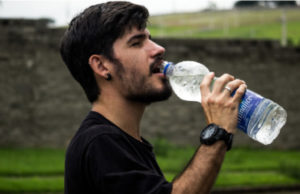 man drinking from a water bottle to benefit his oral health