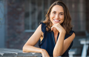 brown haired woman wearing a blue dress smiles after getting porcelain veneers