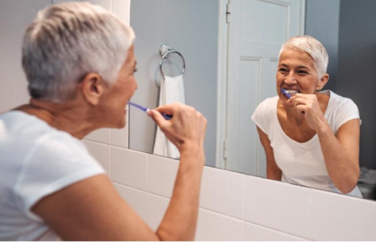 elderly woman looking in the bathroom mirror brushing her teeth