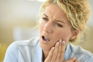 blond woman holds her jaw in pain