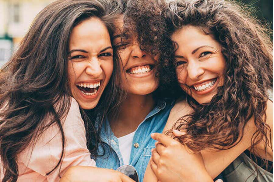 three young women hug and smile showing off their white teeth