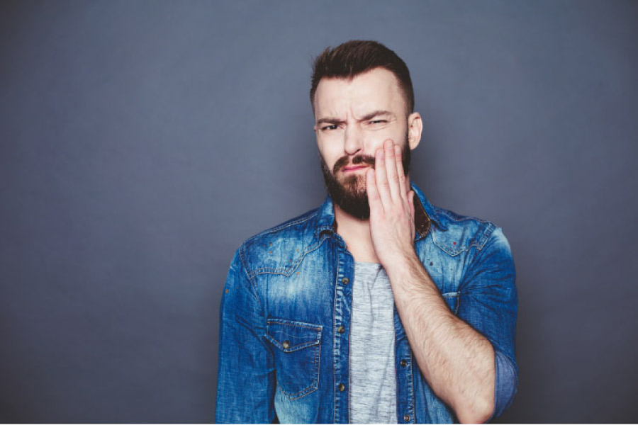 man holds his sore jaw with TMJ disorder